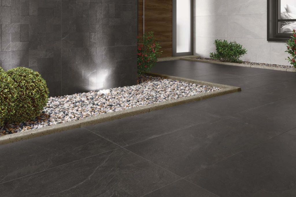 Outdoor dark grey stone effect tiles with feature garden light and gravel.